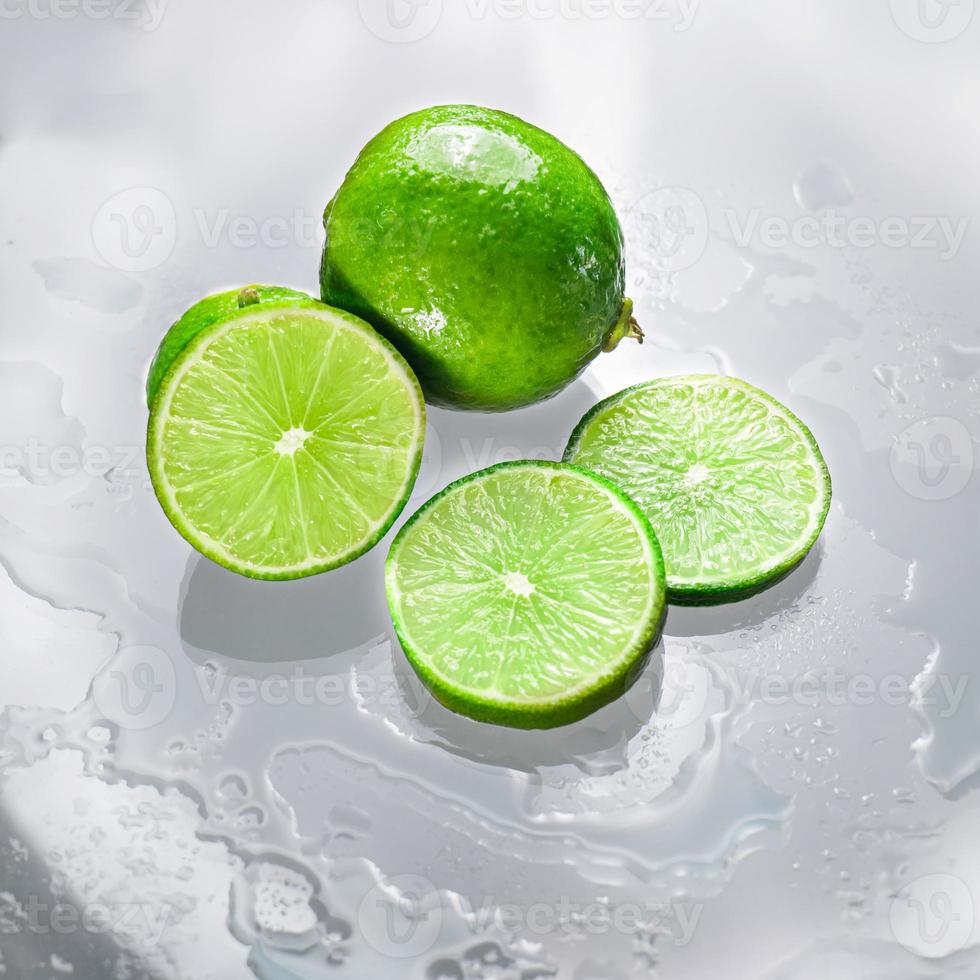de groene limoen is blanco en de gesneden limoenschijf toont de binnenkant van de natte citroenpulp op een helder glazen oppervlak, dat de schaduwen van de limoen en het natte water weerkaatst, waardoor het zijn frisheid krijgt. foto
