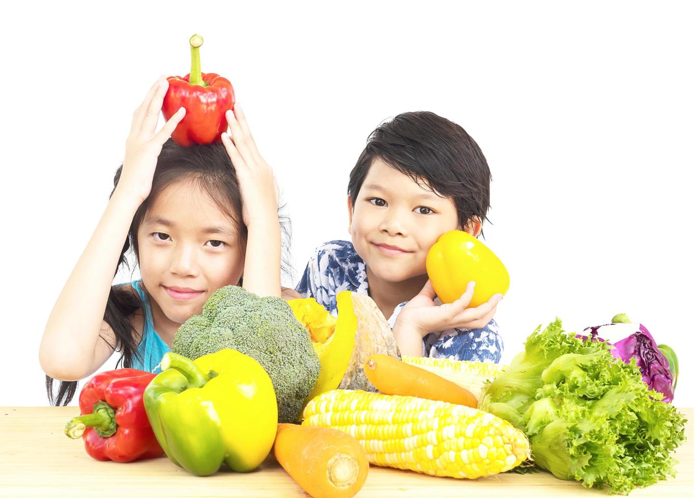 Aziatische jongen en meisje laten zien genieten van expressie met verse kleurrijke groenten geïsoleerd op witte achtergrond foto