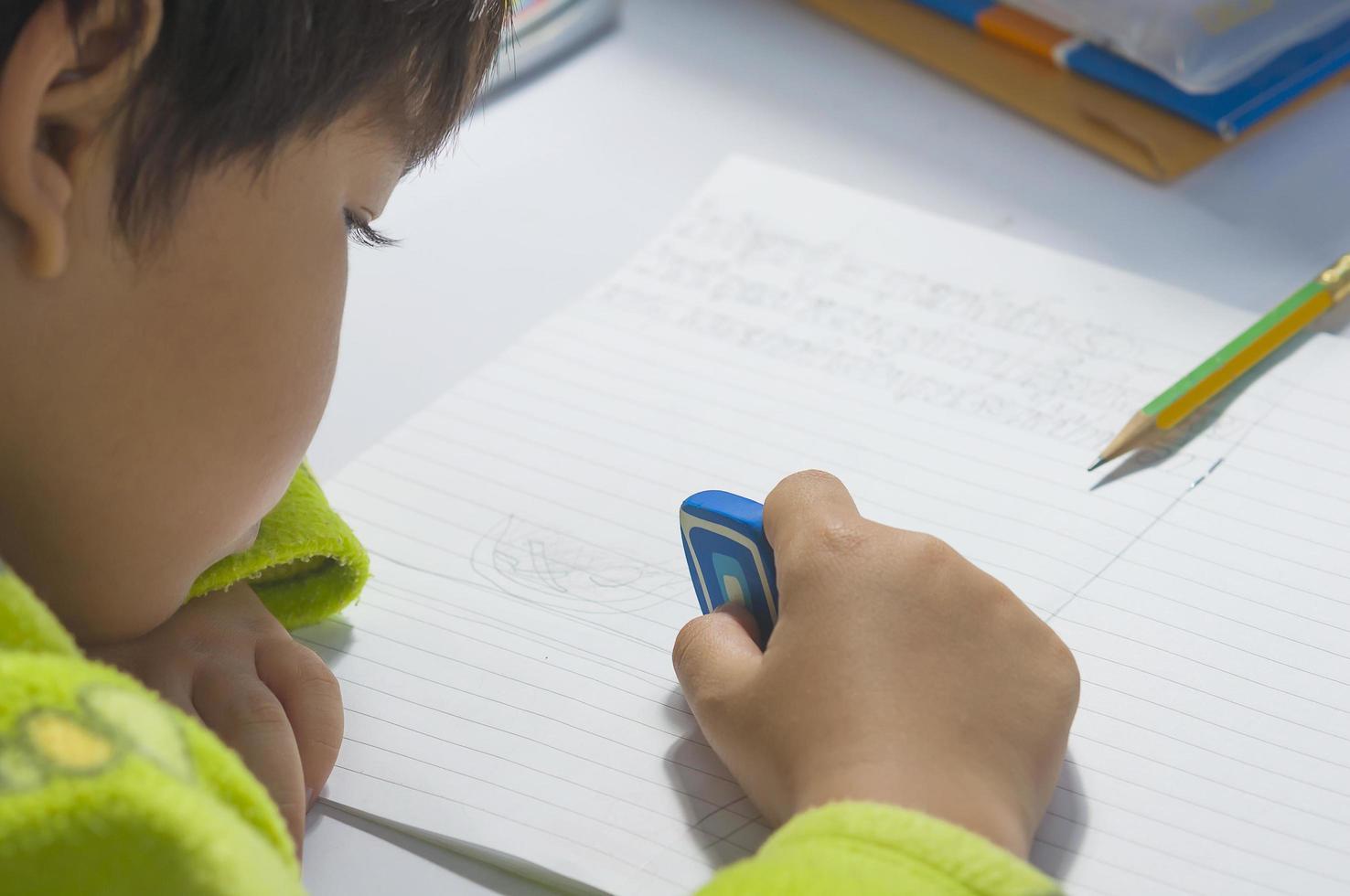 een jongen doet zijn huiswerk en gebruikt een gum foto