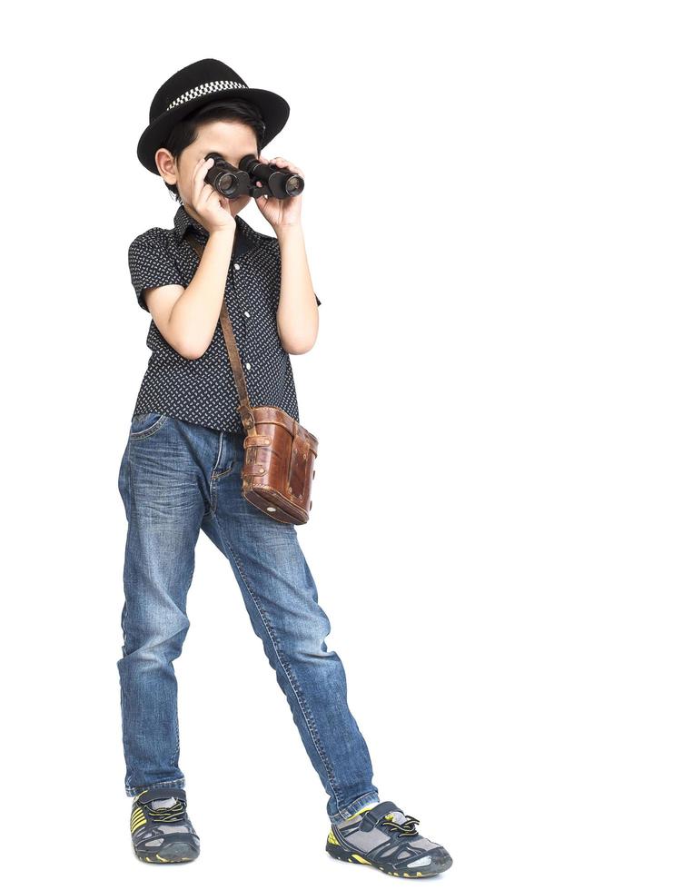 7 jaar oude Aziatische reizigersjongen staat en gebruikt een verrekijker geïsoleerd op een witte achtergrond foto