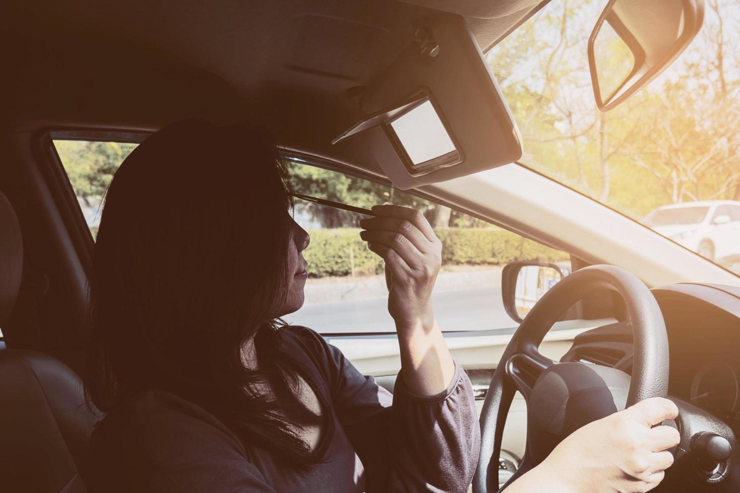 vrouw make-up haar gezicht met wenkbrauwpotlood tijdens het autorijden, onveilig gedrag foto