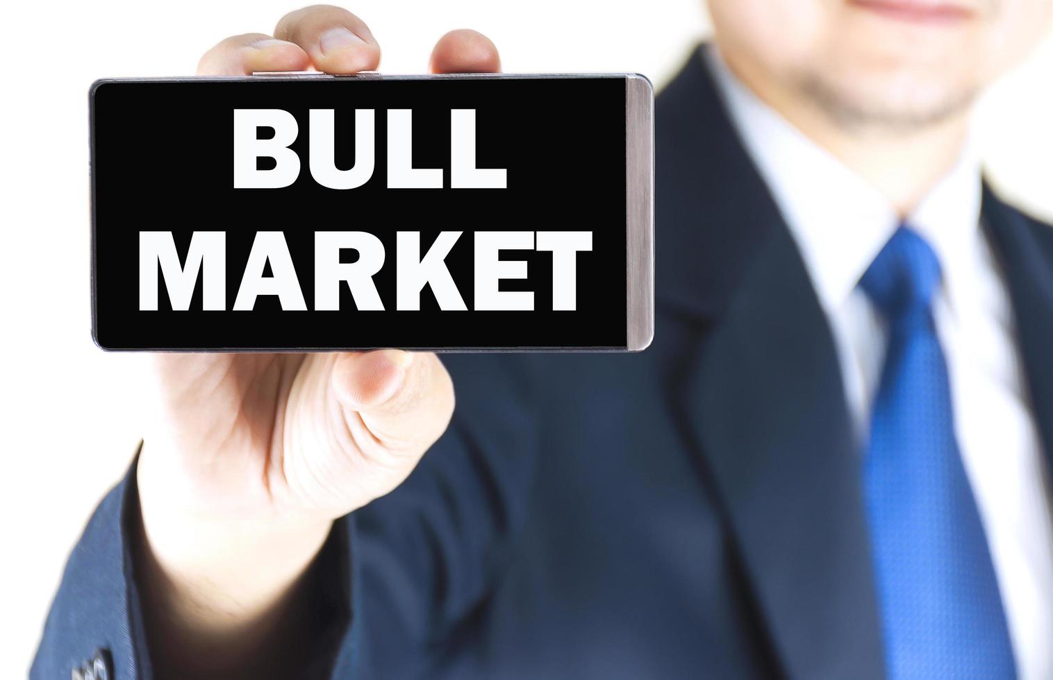 Bull market woord op mobiele telefoon scherm in wazig jonge zakenman hand over witte achtergrond, bedrijfsconcept foto