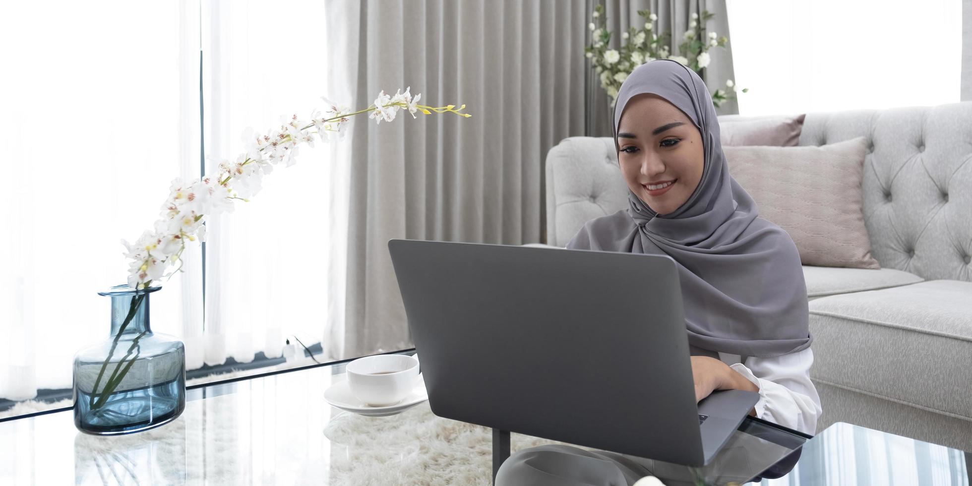 online onderwijsconcept lachende Arabische vrouw met een hoofddoek op haar laptop zit thuis op de achterkant van de bank. geniet van kopieerruimte voor leren op afstand foto