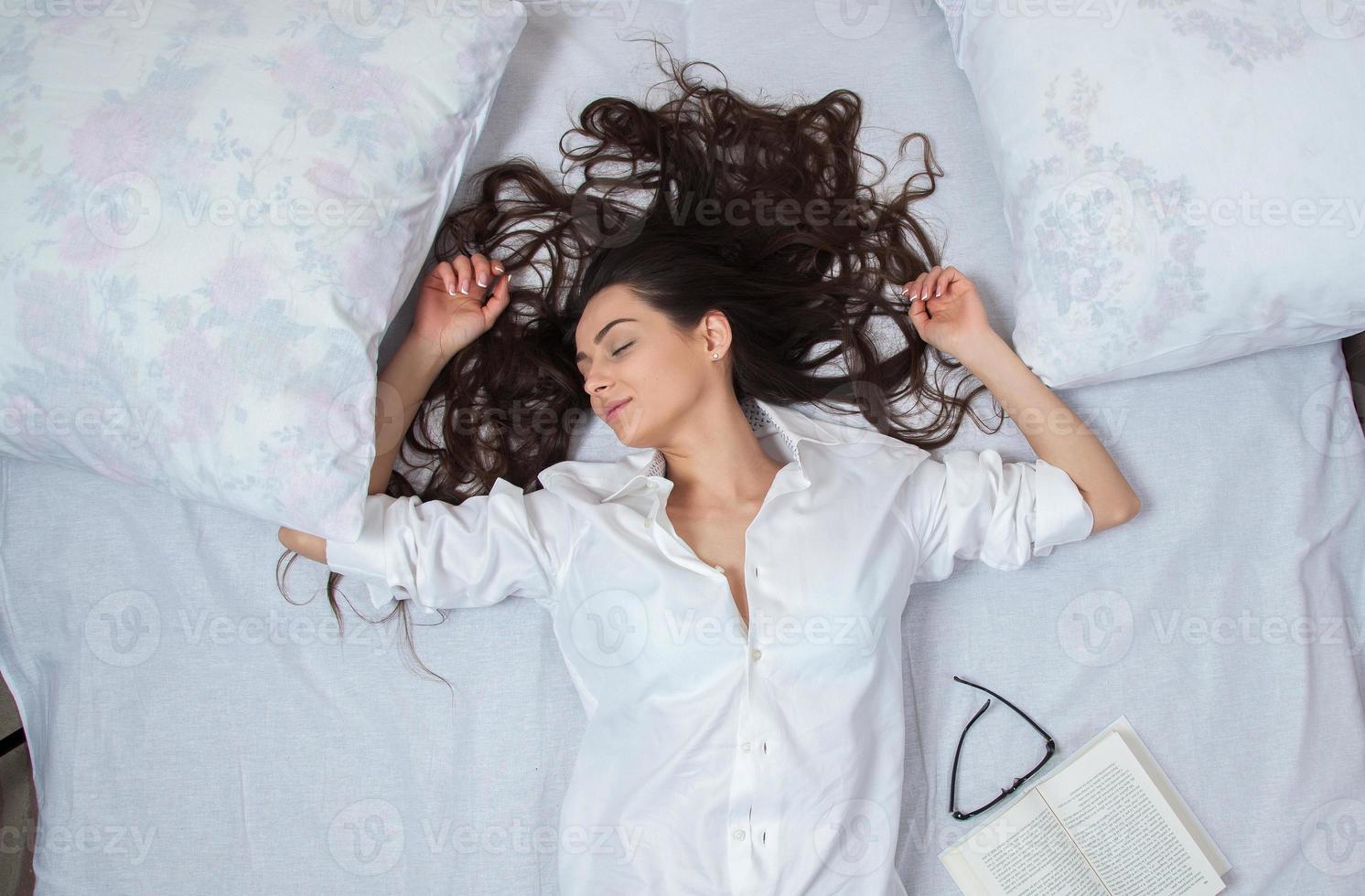 meisje slaapt thuis in een wit bed. jonge vrouw slapen in nachtkleding op het witte linnen in bed thuis, bovenaanzicht. foto
