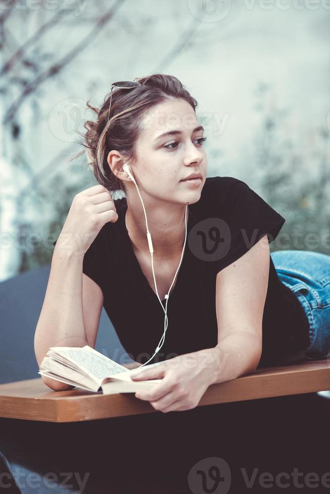 foto van een vrolijk lachend schattig jong studentenmeisje dat buiten een zonnebril draagt met behulp van een mobiele telefoon die naar muziek luistert met oortelefoons.