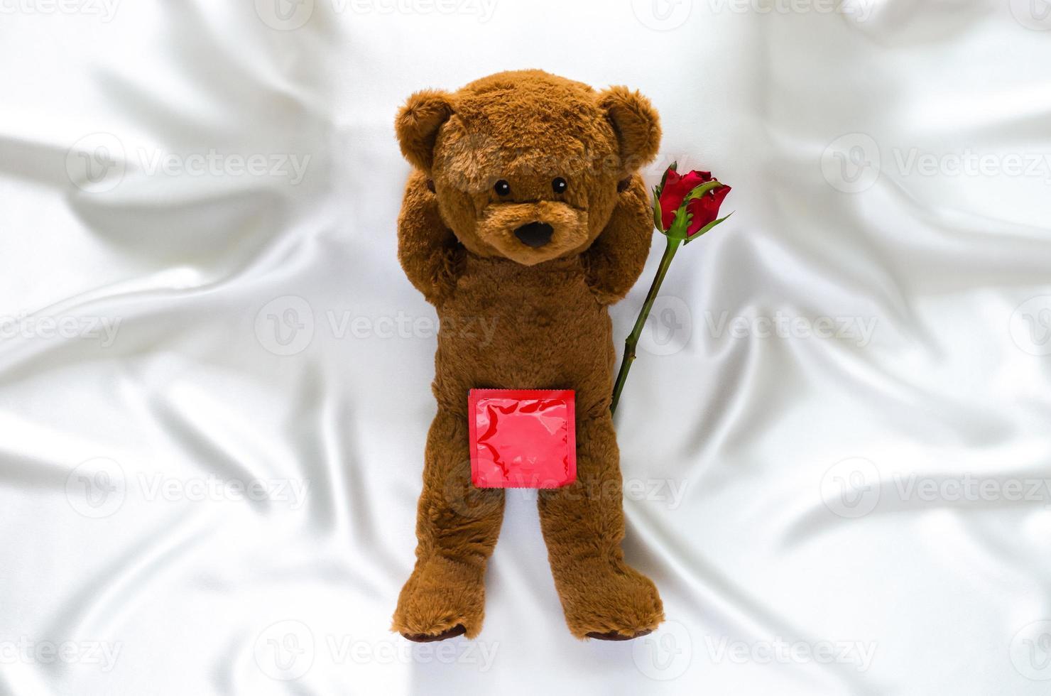 teddybeer liggend op bed met roos en condoompakket voor veilige seks, wereld seksuele gezondheid en aids-dagconcept. foto