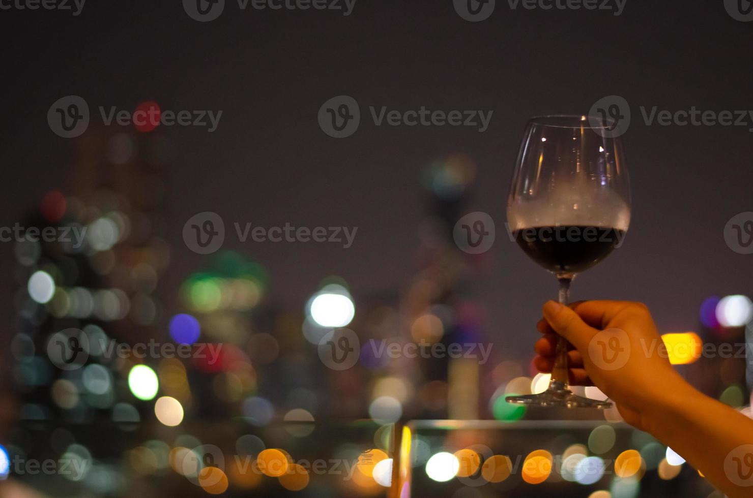 hand vasthouden en roosteren van een glas rode wijn in de bar op het dak. foto