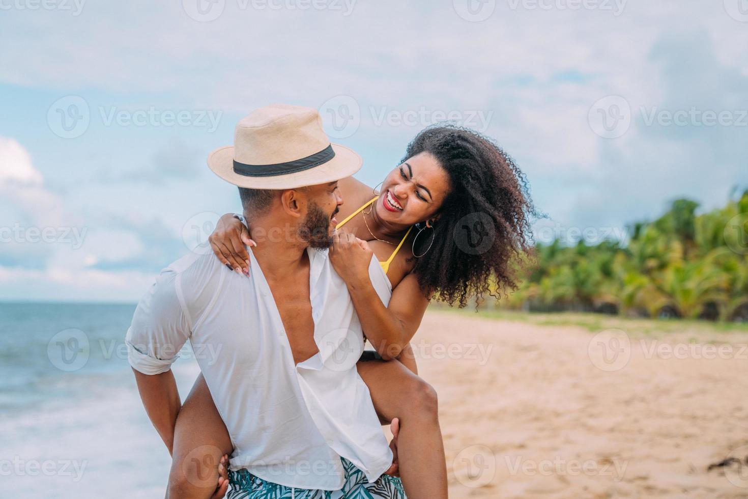 jong stel op strand zomervakantie, gelukkig lachende man draagt vrouw terug aan zee foto