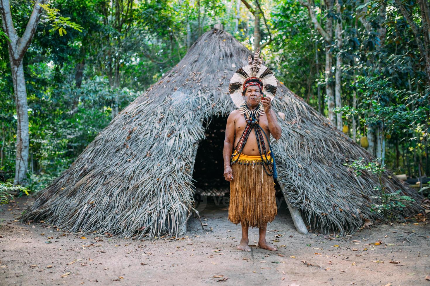 sjamaan van de pataxo-stam, gekleed in veren hoofdtooi en pijp rokend. Braziliaanse indiaan die naar de camera kijkt foto