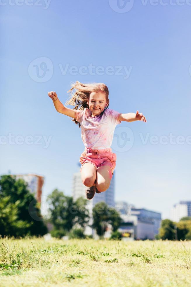 klein meisje springt hoog in het stadspark in kleurrijke vuile kleren. foto