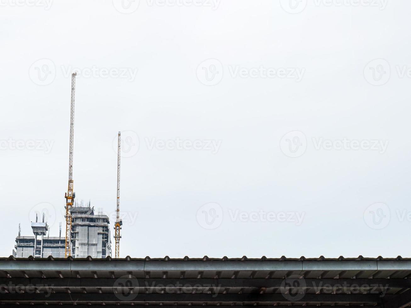 twee bouwkranen werken aan de constructie van hoge gebouwen, hijsen en plaatsen dingen. de bouwplaats is bedekt met dekens. in de witte lucht stad gebouw in een rechte lijn foto