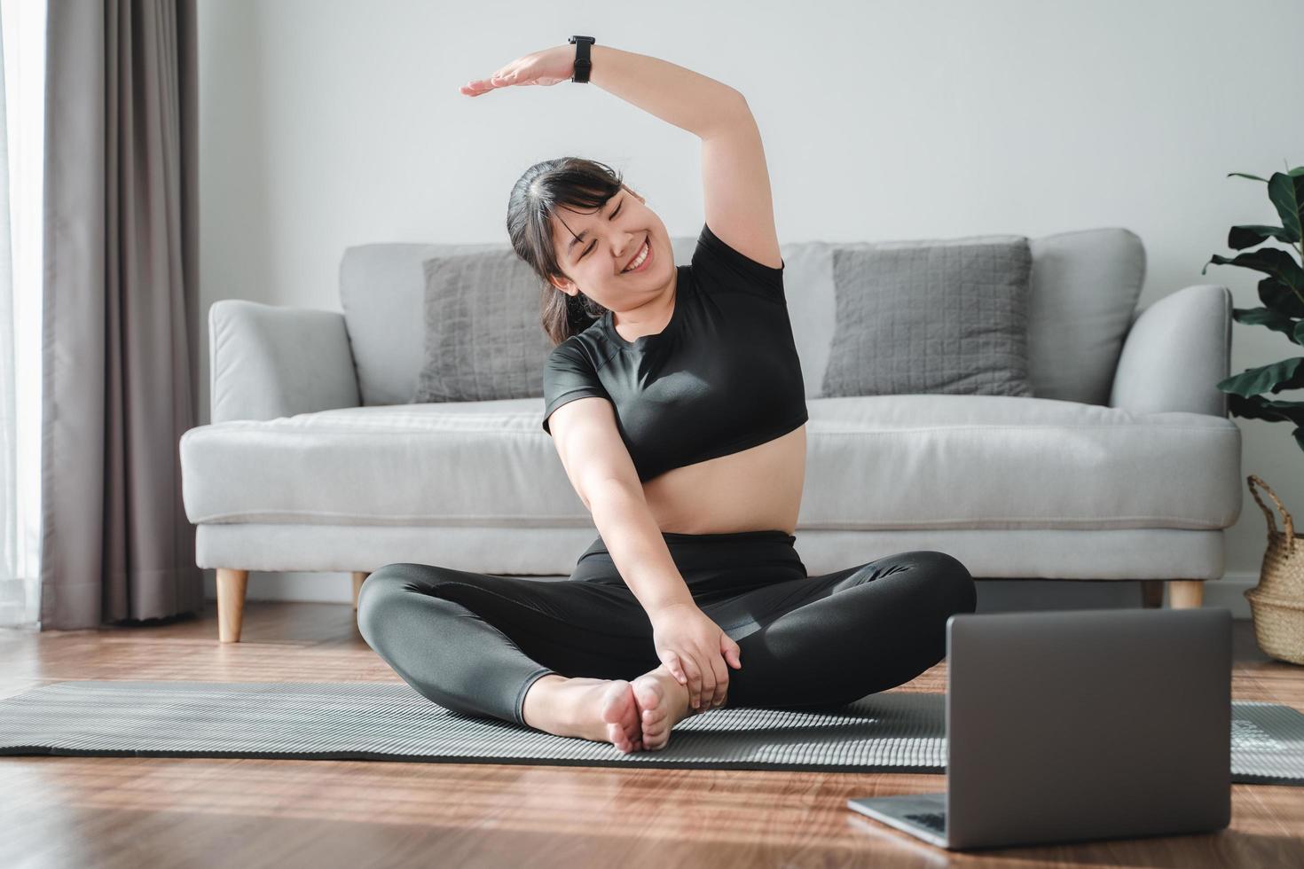 Aziatische mollige vrouw zittend op de vloer in de woonkamer oefen online yogales met de computer. vrouw met mediteren trainingsklasse op de laptop. foto