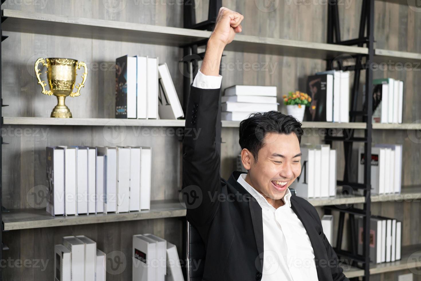 werknemer werkgever werkgelegenheid ondernemer uitvoerende man in formalwear opgeheven handen vuisten zitten op stoel. emotionele man die zich blij en gelukkig voelt omdat hij groot succes is, succesvolle zaken afrondt. foto