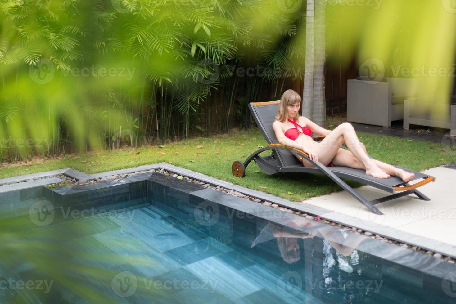 vrouw ontspannen op chaise longue bij zwembad. foto