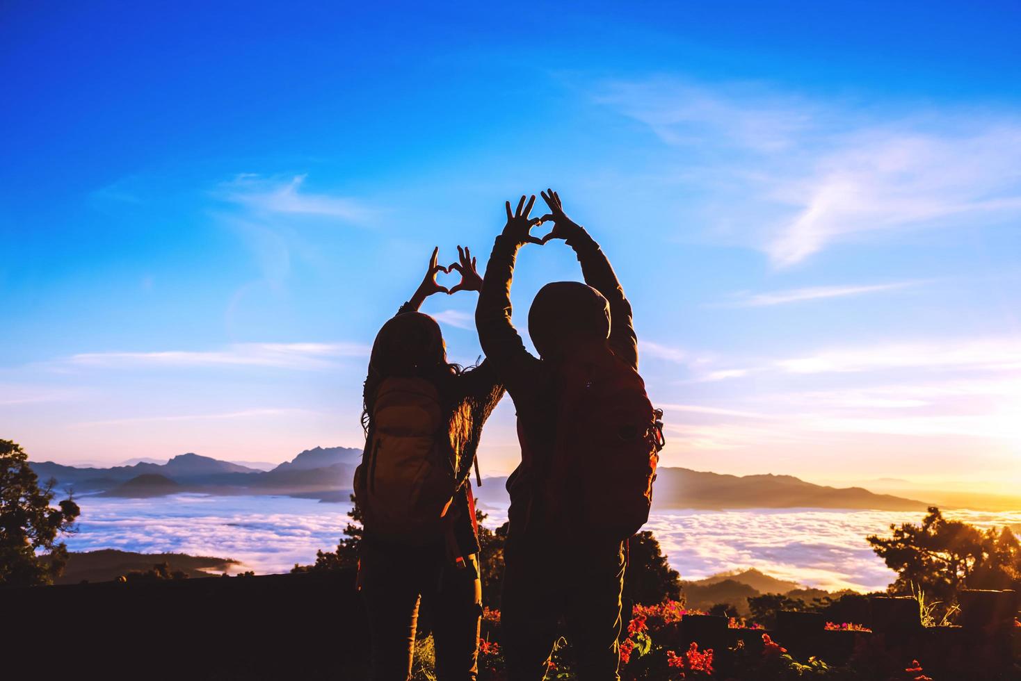 minnaar vrouwen en mannen aziaten reizen ontspannen in de vakantie. sta op voor zonsopgang op de berg, gelukkige huwelijksreis, hief zijn hand op om een hartvorm te maken. foto