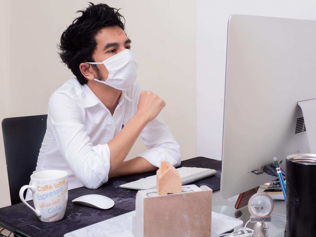 jonge aziatische jongen met gezichtsmasker die op een laptop werkt tijdens een pandemie van het coronavirus foto