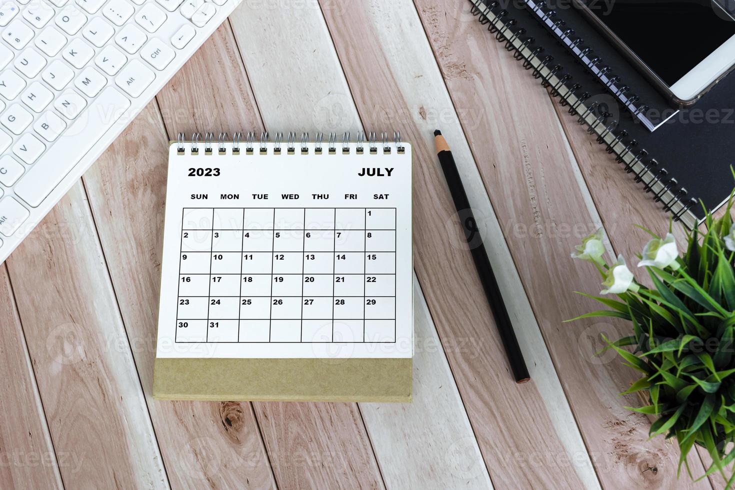 witte juli 2023 bureaukalender op houten bureau. recht boven. plat liggen. foto