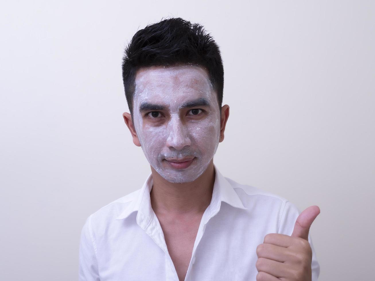 Aziatische knappe jongeman die crème op zijn gezicht aanbrengt met smileygezicht, huidverzorgingsconcept foto