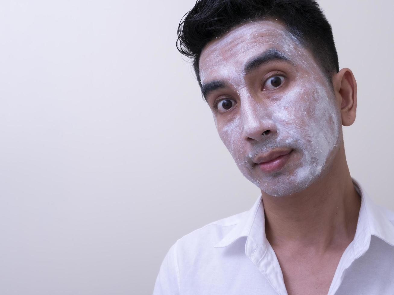 Aziatische knappe jongeman die crème op zijn gezicht aanbrengt met smileygezicht, huidverzorgingsconcept foto