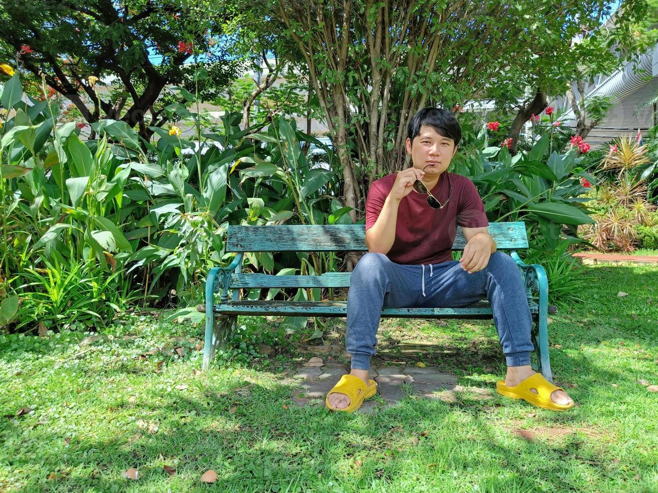 jonge aziatische man met zwart haar zit op een bankje met een zonnebril. wat denk je in het stadspark foto