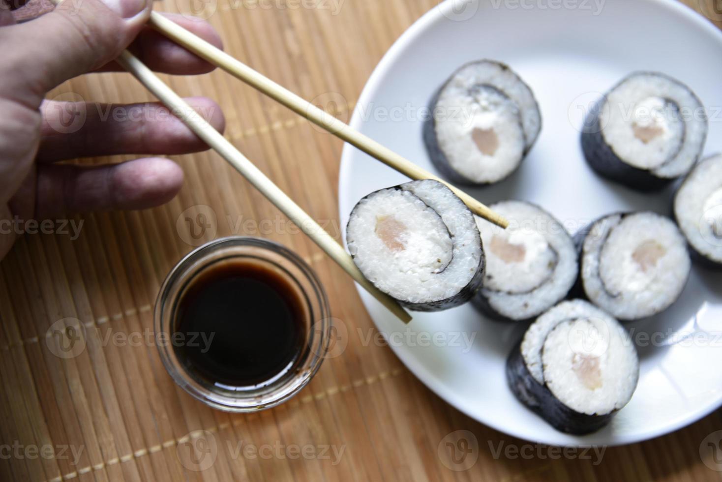 genomen met stokjes sushi met tonijn om te eten. heerlijke visrol. rijst sushi roll op een mat. foto