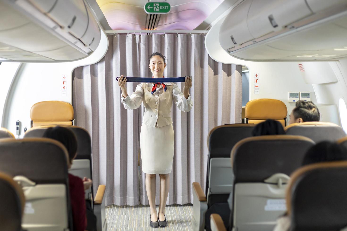 Aziatische stewardess demonstreert veiligheidsprocedure met veiligheidsgordel voordat hij opstijgt in het vliegtuig voor cabinepersoneel en luchtvaartbedrijfsconcept foto