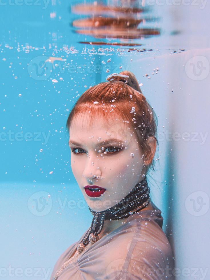 surrealistisch kunstportret van een jonge vrouw in een grijze jurk en een sjaal met kralen onder water in het zwembad foto