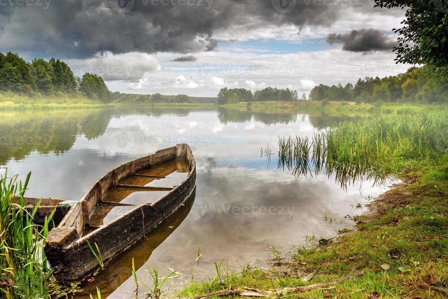 oude houten boot aan de oever van een brede rivier in bewolkte dag voor de storm met mist foto