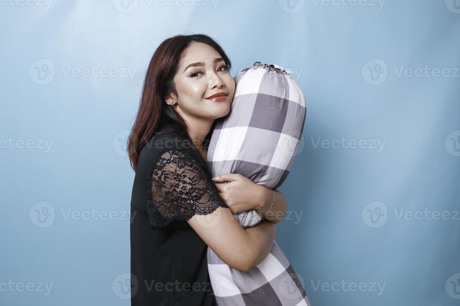portret van slaperige aantrekkelijke aziatische vrouw die een pyjama draagt, glimlacht en steun vasthoudt foto