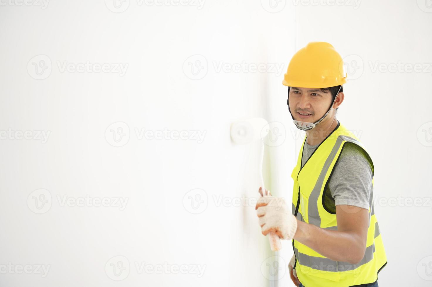 een aanzicht van de schilder achter de muur schilder met een verfroller en gespleten emmer op een grote lege ruimte met een houten trap. foto