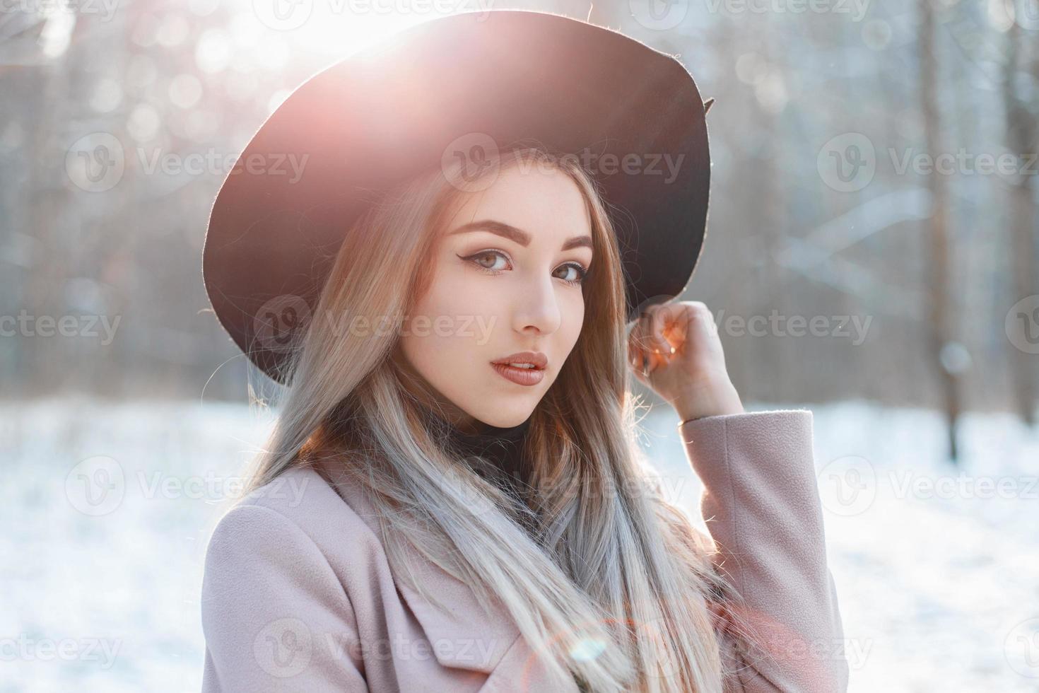 portret van een jong mooi meisje met een zwarte hoed op een winterdag bij zonsondergang foto