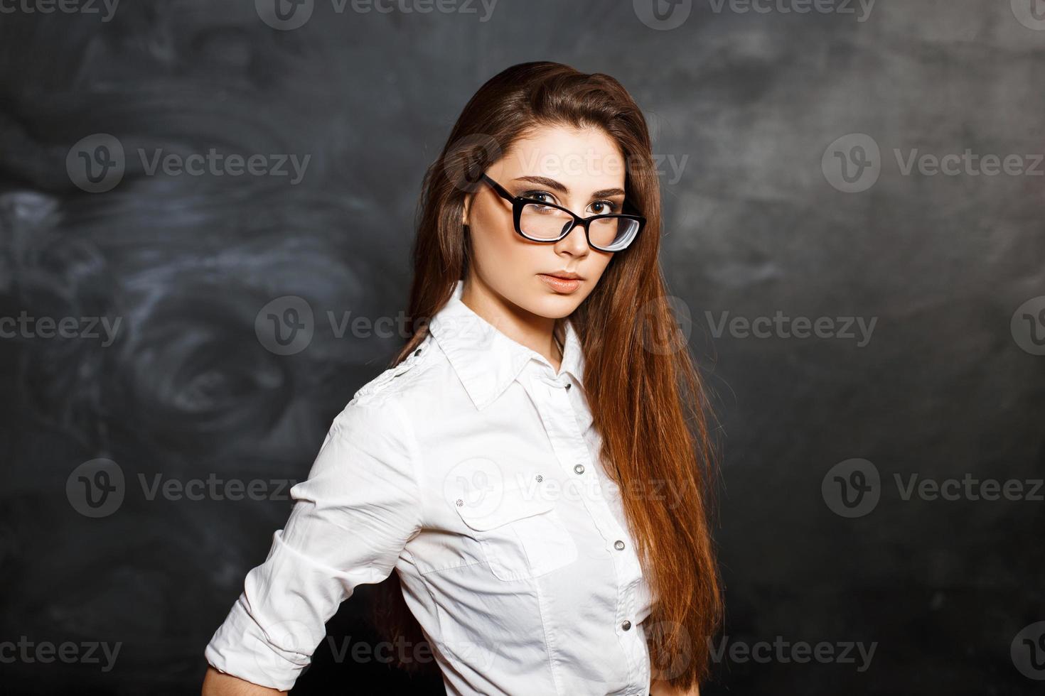 close-up portret van een jong mooi meisje met stijlvolle bril en een witte blouse op een donkere achtergrond. foto