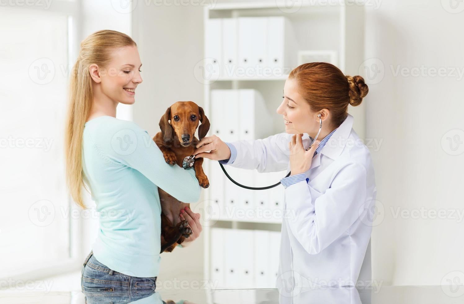 gelukkige vrouw met hond en arts bij dierenartskliniek foto