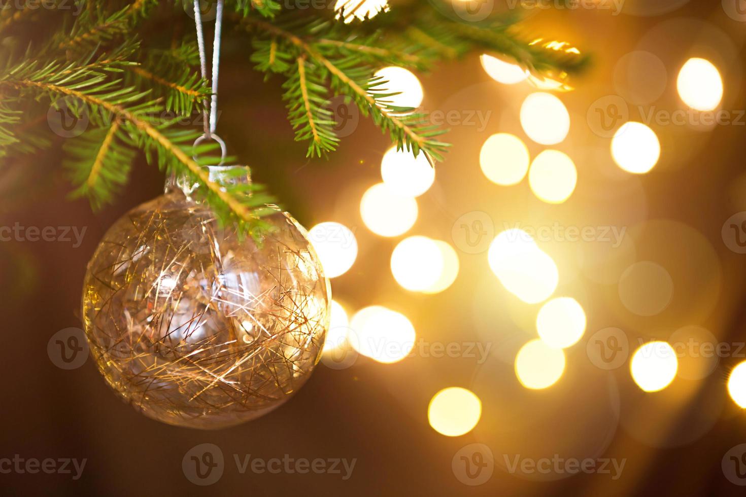 gouden kerstbal op een levende tak van een dennenboom met gouden lichten van slingers in defocus. nieuwjaar, kerstmis, vakantieachtergrond, bokeh, kopieer ruimte foto