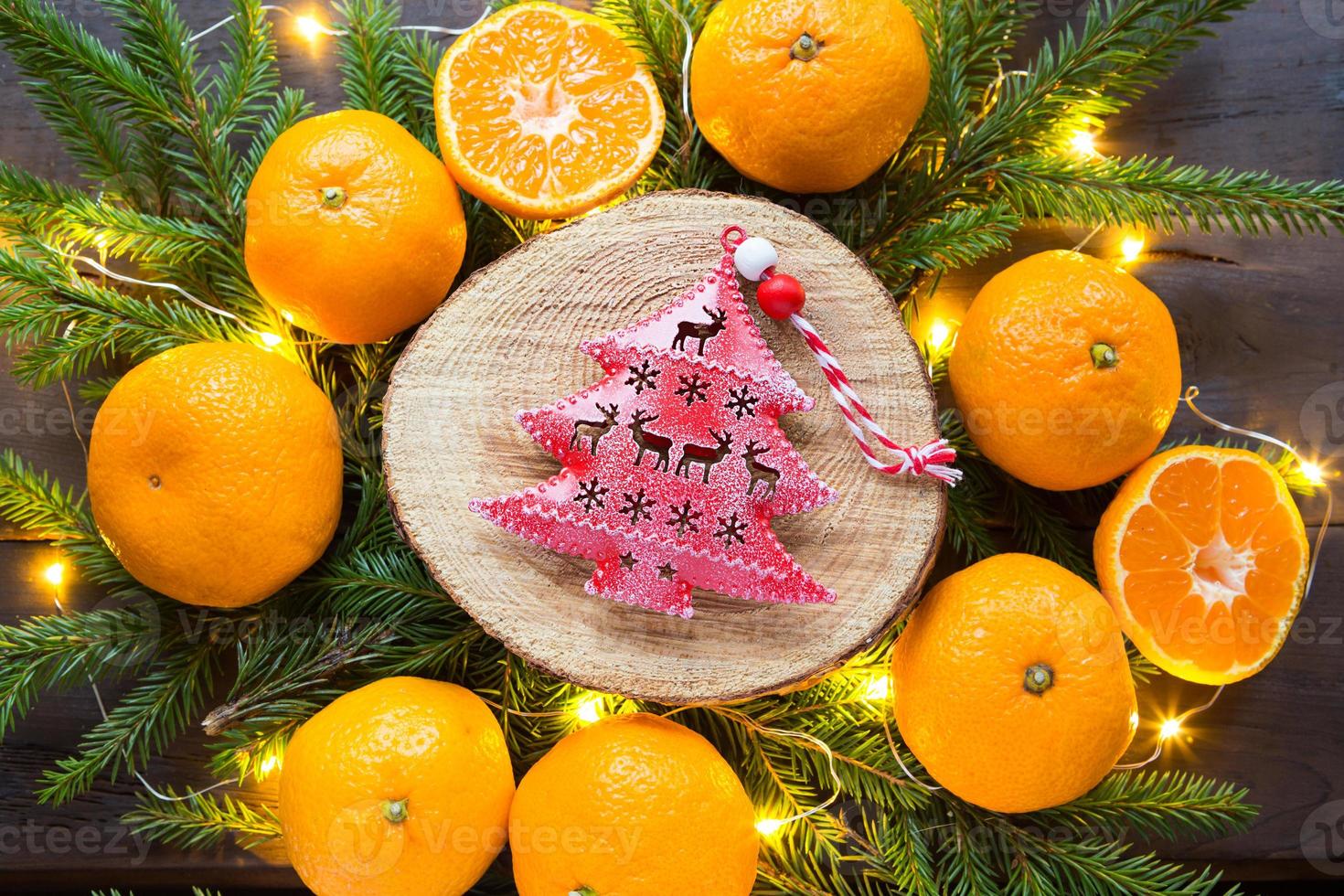 rood kerstboomspeelgoed op ronde snede van een boom omringd door mandarijnen, levende dennentakken en gouden lichtslingers. citrusaroma, schijfjes sinaasappel, kerstmis. frame, nieuwjaarsvakantie achtergrond foto