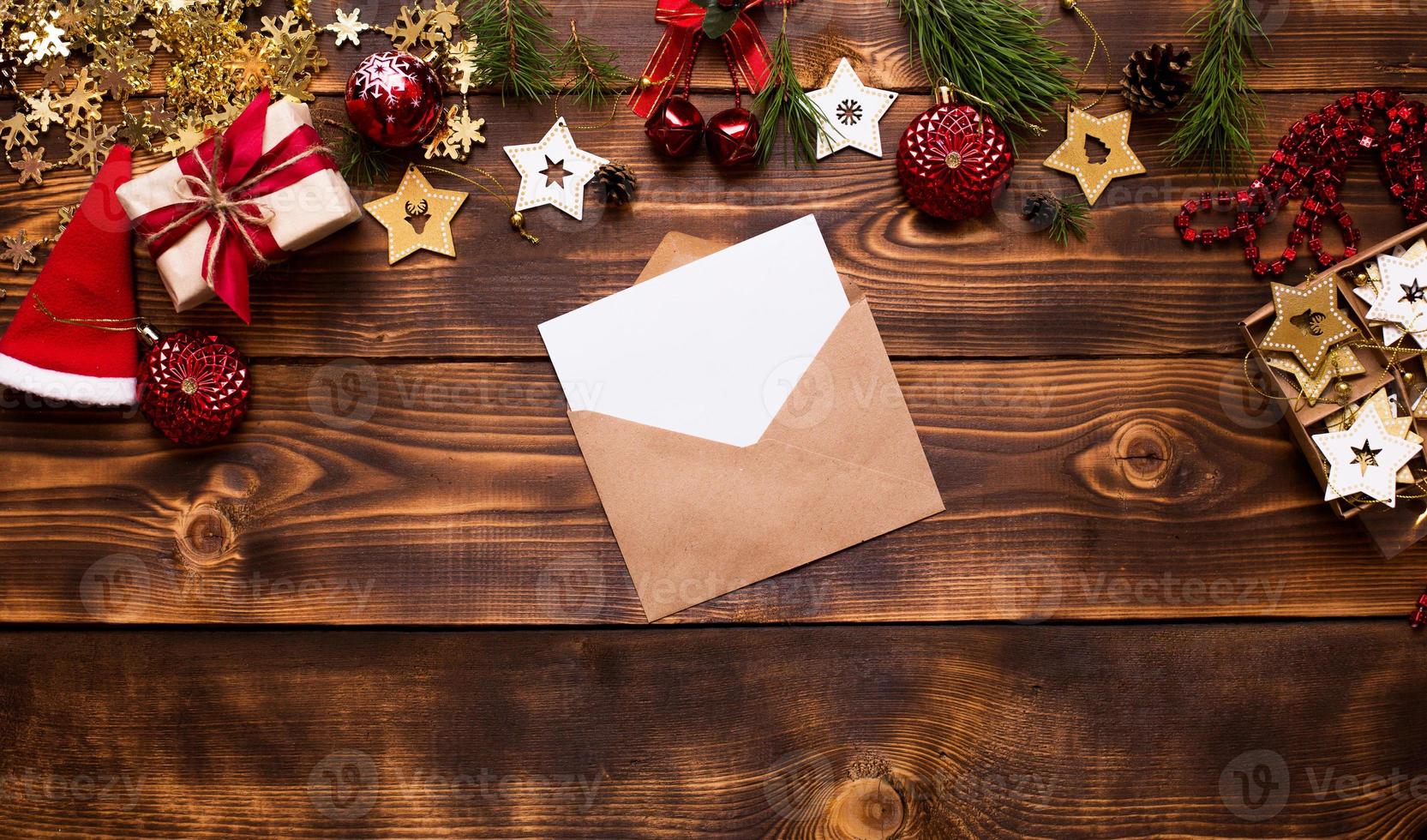 mail envelop gemaakt van ambachtelijk papier met een wit vel voor tekst op een houten achtergrond met kerst decor. een brief aan de kerstman, een verlanglijstje, een nieuwjaarsdroom, een cadeau. plat leggen, ruimte kopiëren foto