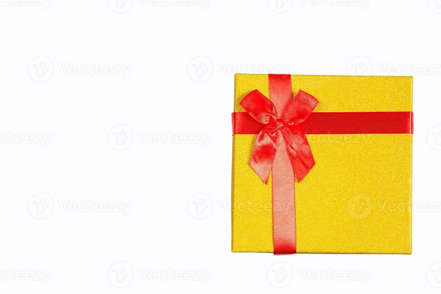 de gouden geschenkdoos is vastgebonden met een rood lint met een strik op een witte achtergrond en geïsoleerd. ruimte kopiëren. cadeau voor Kerstmis, Nieuwjaar, verjaardag, vakantie. foto
