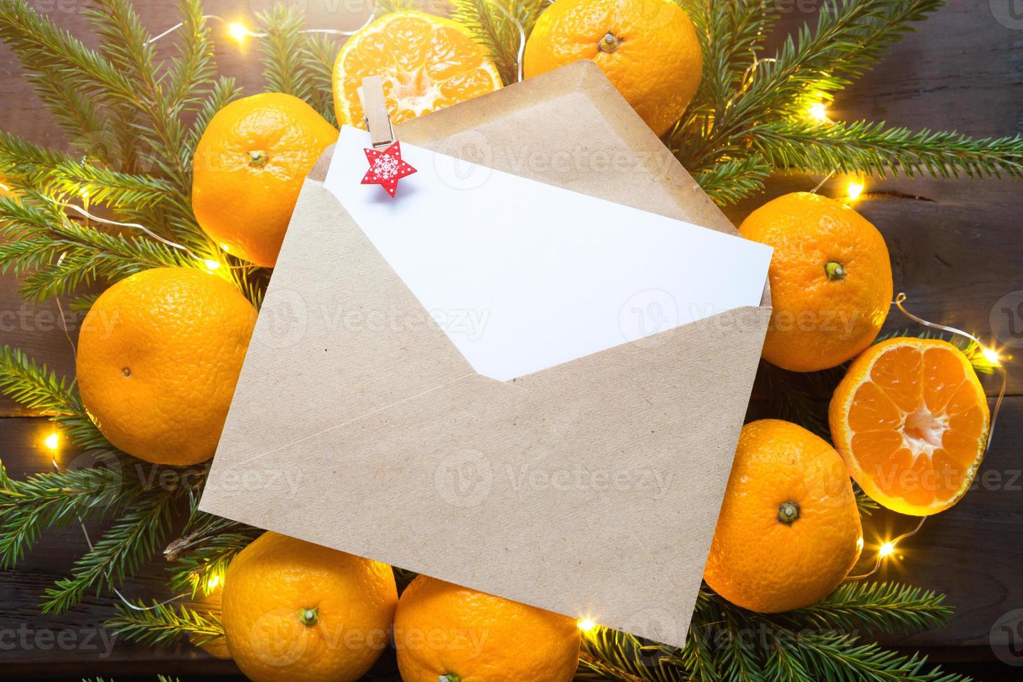 envelop met een vel papier - een brief aan de kerstman, copyspace op een kerstachtergrond van mandarijnen, slingers, dennentakken. wasknijper-ster op zijn plaats voor notities. nieuwjaar, verlanglijstje, droom, cadeaus foto