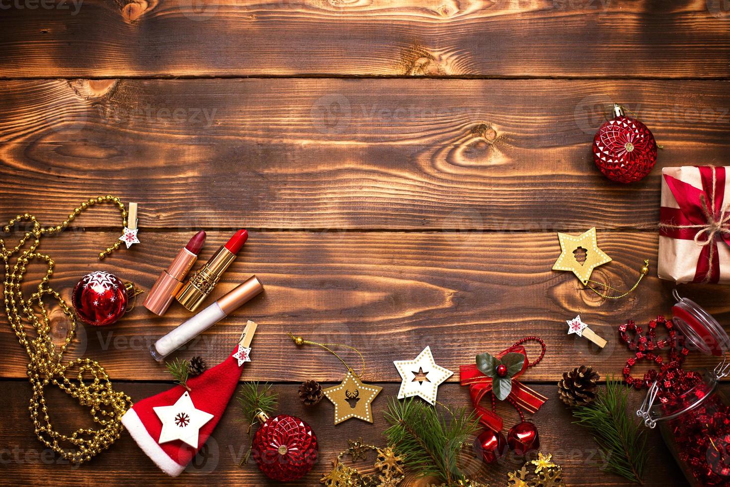 rode lippenstift en lipgloss en oogleden op een houten ondergrond in het kerstdecor. vakantie make-up voor het nieuwe jaar, cadeau, winkelen, verlangens van vrouwen. ruimte voor tekst, plat gelegd foto