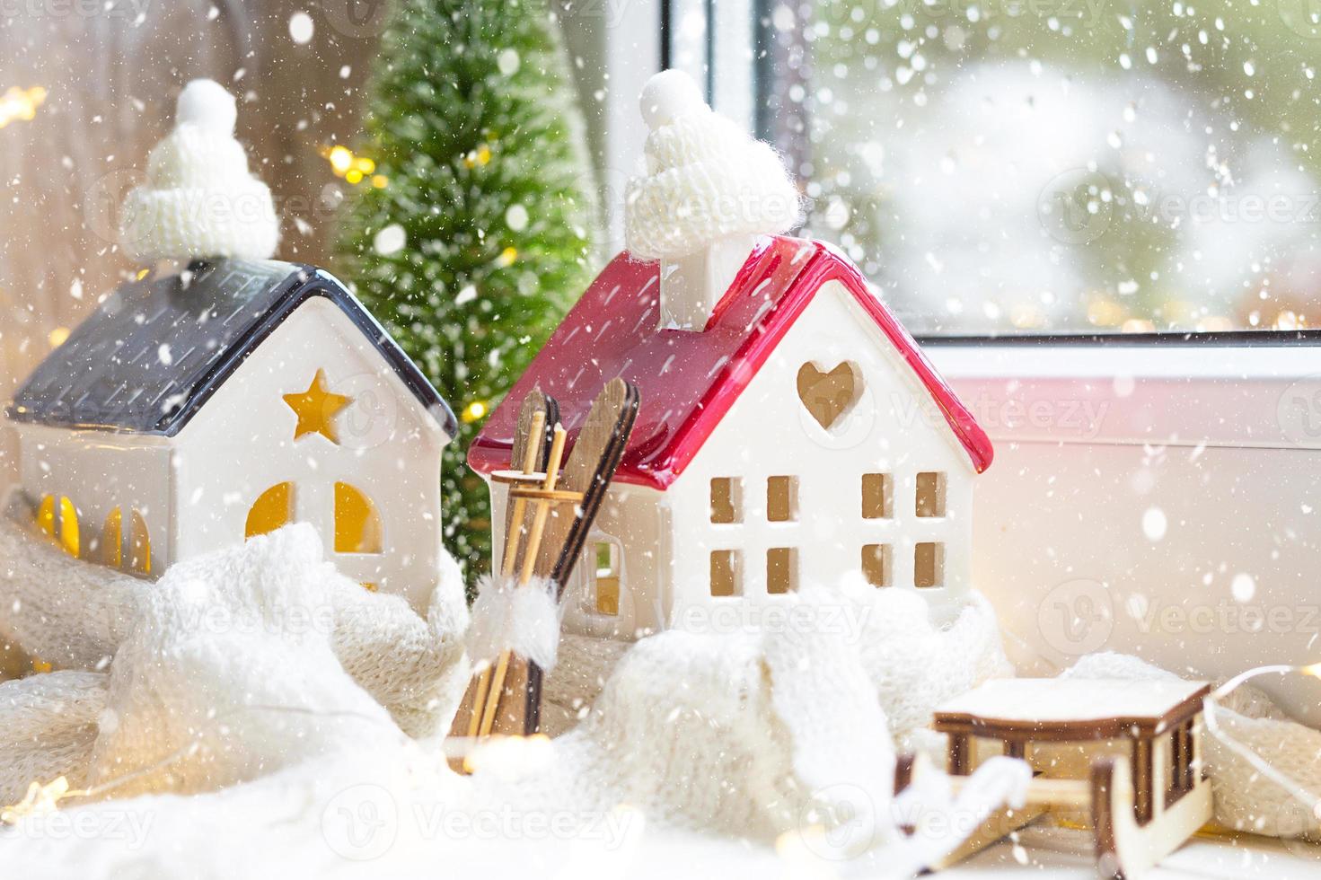 gezellig huis is gewikkeld in een muts en sjaal in een sneeuwstorm -vensterbank decor voor kerstmis, nieuwjaar. winter, sneeuw - woningisolatie, bescherming tegen kou en slecht weer, verwarmingssysteem. Feestelijke stemming foto
