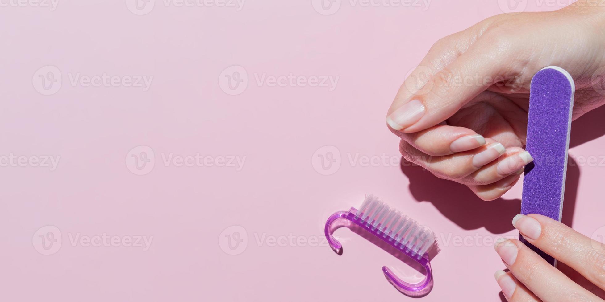 stijlvolle mooie manicure. handen van jonge vrouw met nagelvijl, manicure tools op roze achtergrond bovenaanzicht plat lag. natuurlijke nagels zelfzorg schoonheid en mode. nagelverzorging salon spa thuis. banier foto