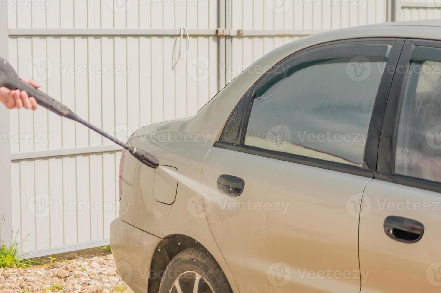 man die zijn auto buiten onder hoge druk wast foto