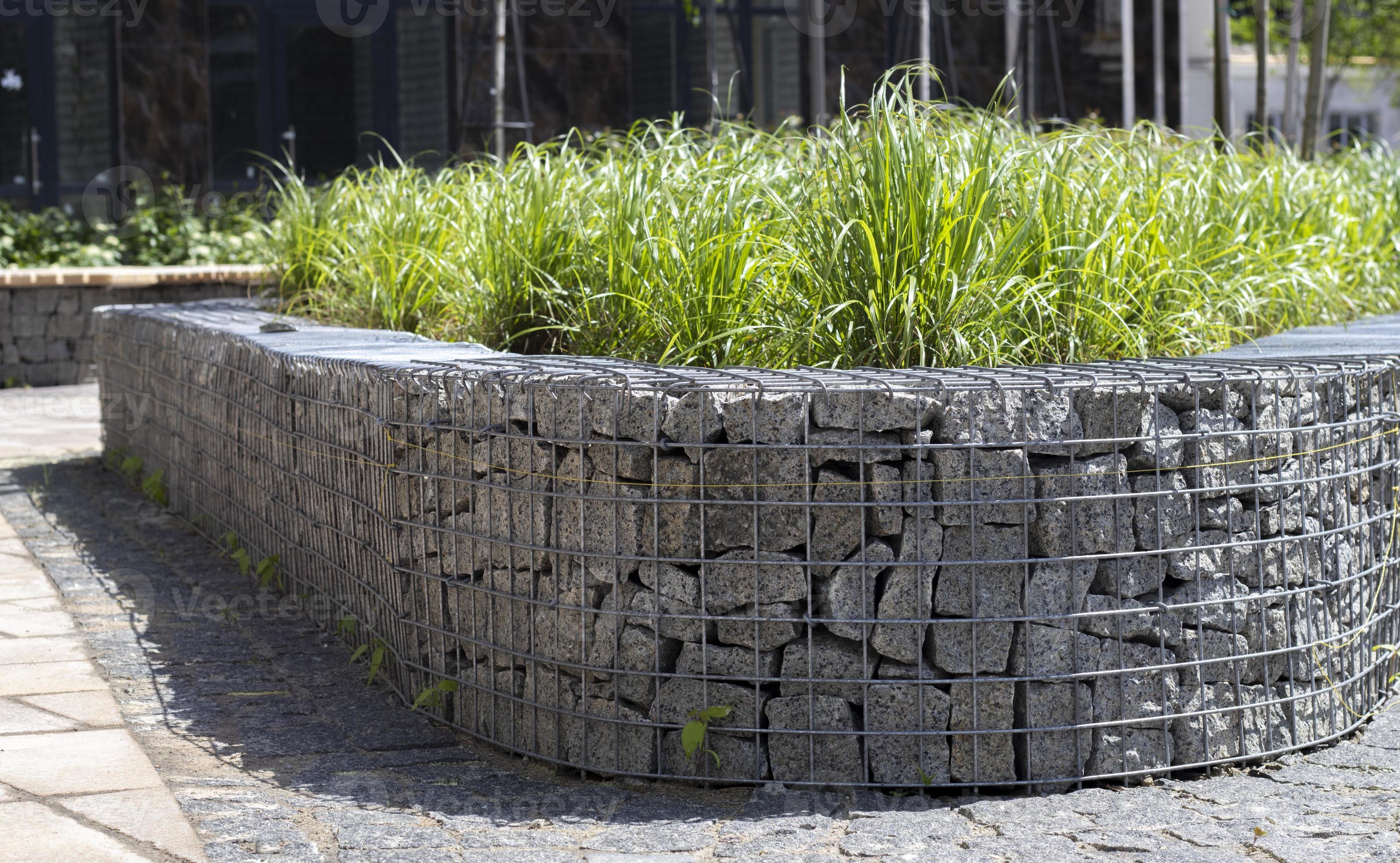 mand ondersteuning muur gemaakt van graniet schanskorf. schanskorven in de tuin. modern schanskorf hek met stenen in draad gaas. draad maas hekwerk met natuurlijk steen en struiken. 10618580 Stockfoto