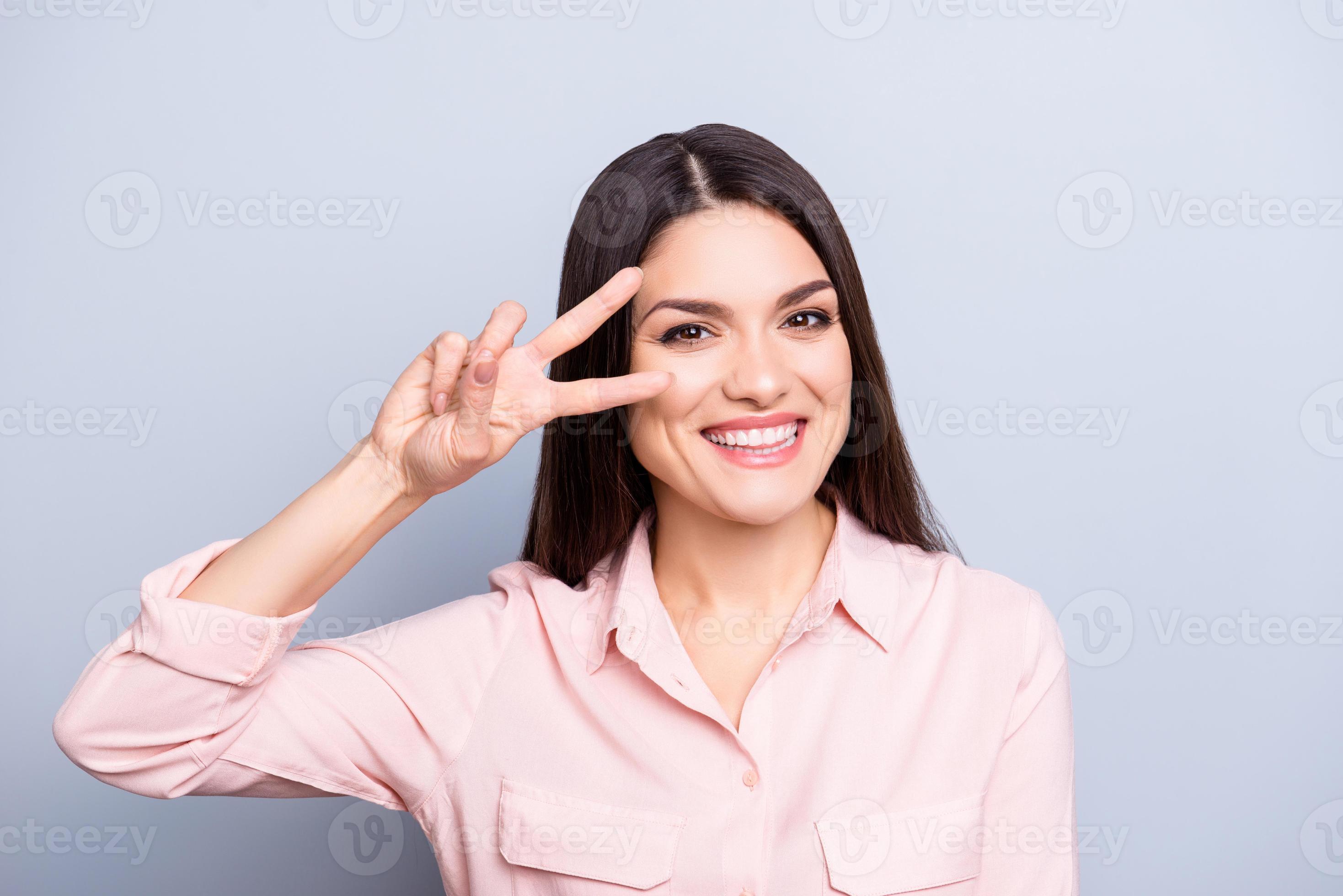 Portret van speelse, funky, mooie, mooie, charmante vrouw in goed humeur gebaren v-teken met twee vingers in de buurt van oog kijken camera geïsoleerd op grijze achtergrond foto