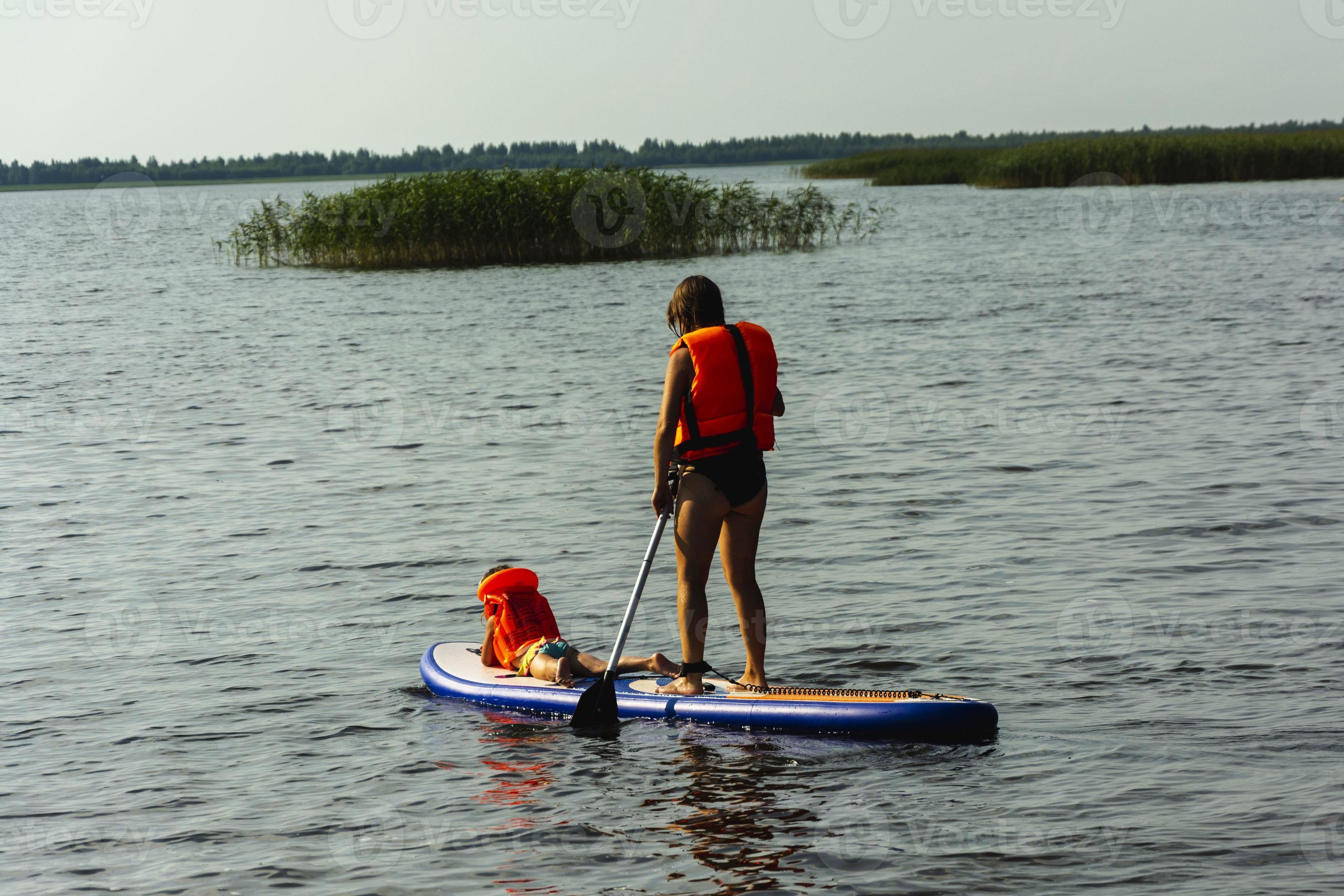 een jong moeder zwemt Aan een staand peddelen bord met haar weinig dochter.  sup bord. water sport- 14706630 stockfoto bij Vecteezy