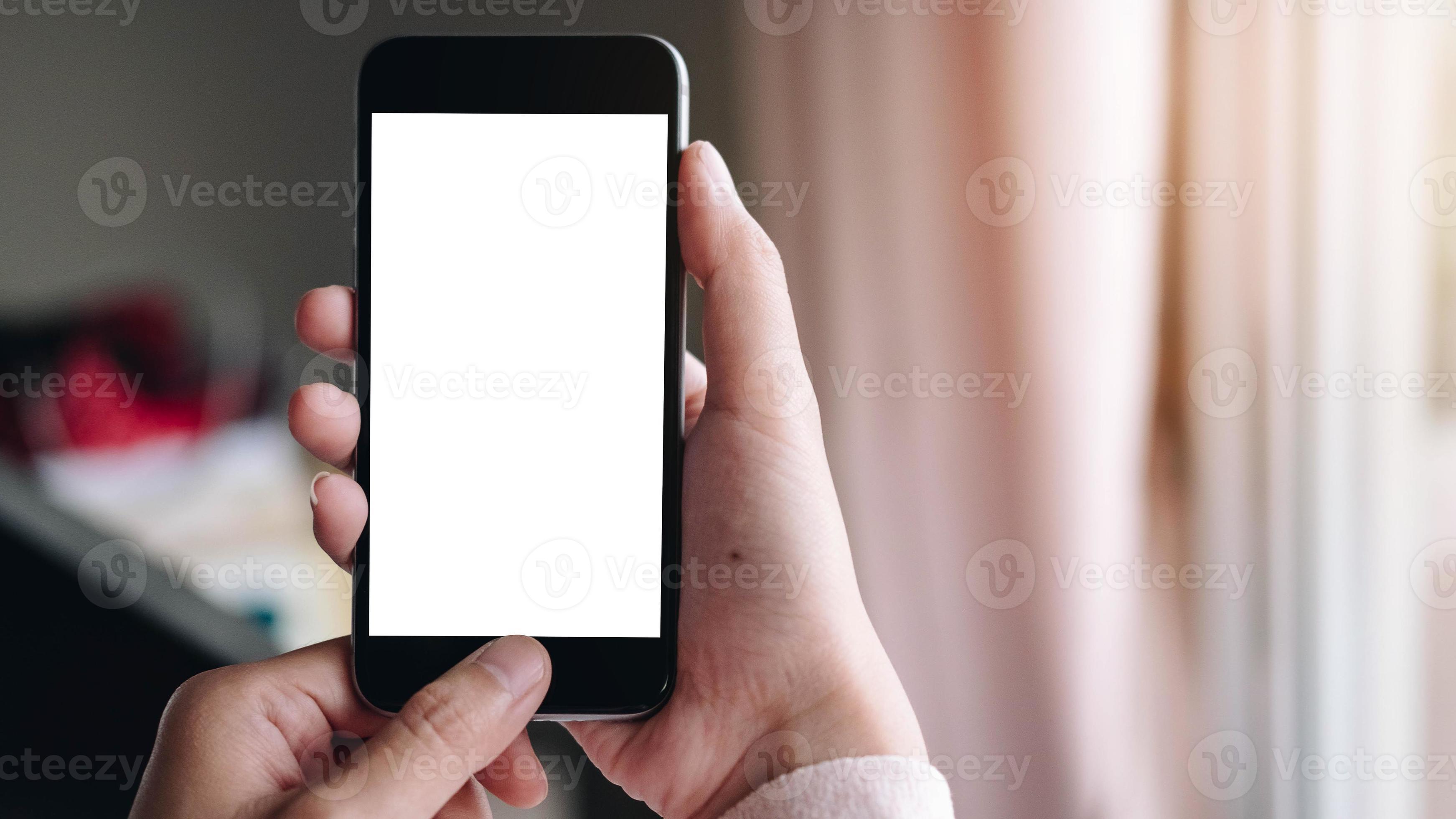 close-up van de hand van een vrouw met behulp van een slimme telefoon met een leeg scherm thuis foto