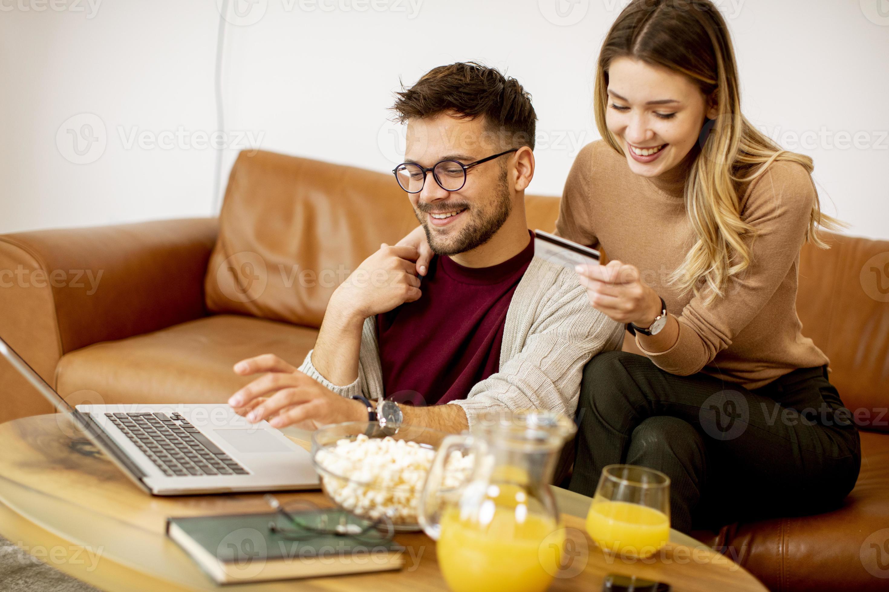 jonge vrouw en jonge man met behulp van laptop voor online betaling zittend op de bank thuis foto