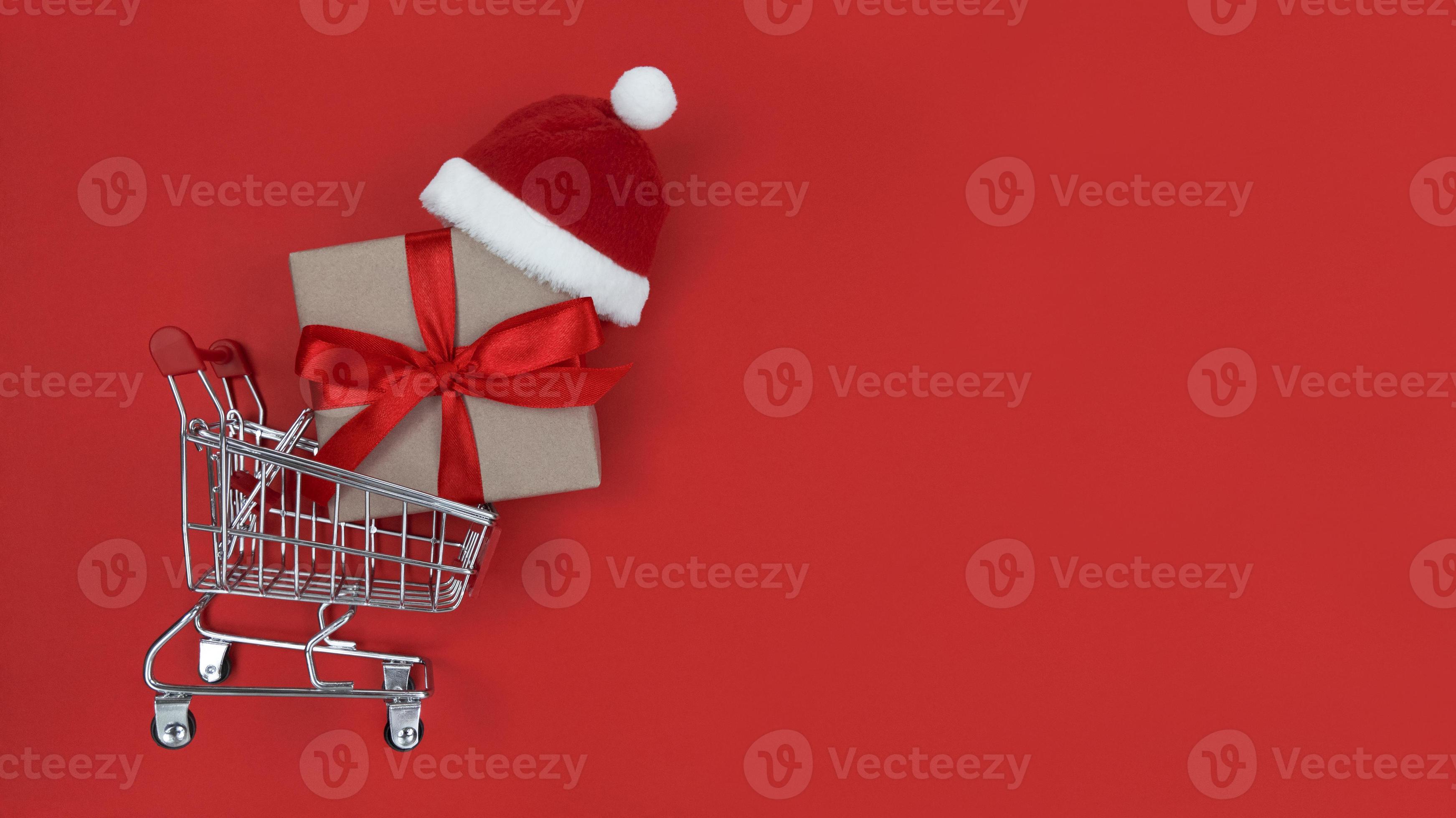 supermarktkarretje, geschenkdoos en kerstmuts op een rode achtergrond. foto