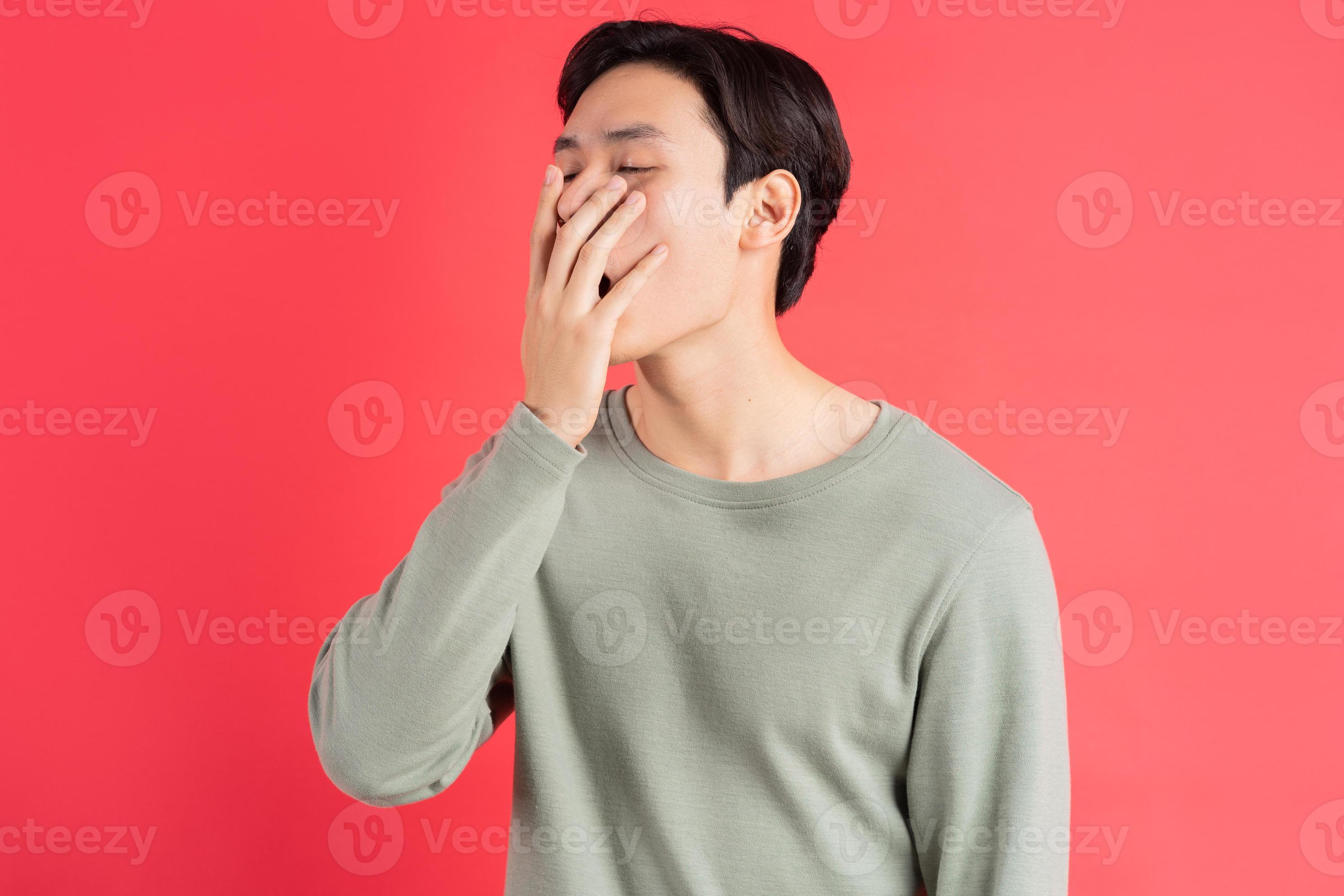 een foto van een knappe Aziatische man die geeuwt met zijn hand voor zijn mond