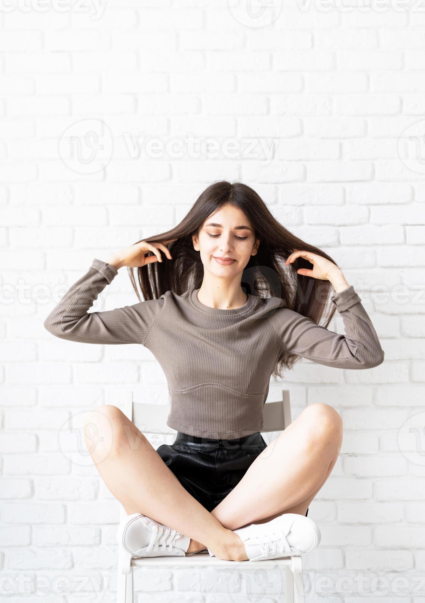 brunette vrouw met lang haar zittend op witte bakstenen muur achtergrond foto